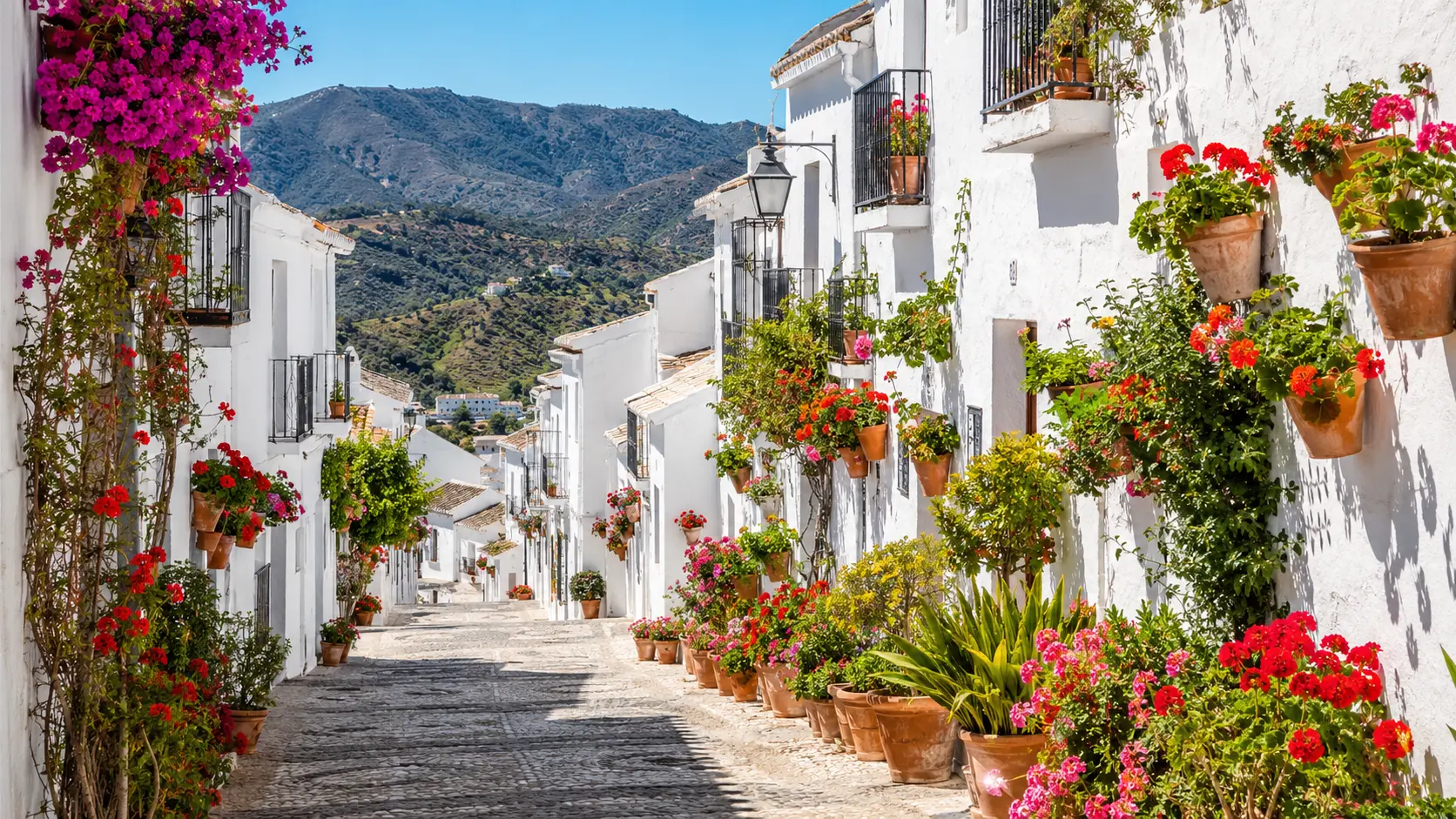 Callejuelas blancas de Frigiliana en primavera con macetas de flores y vistas a la sierra de la Axarquía